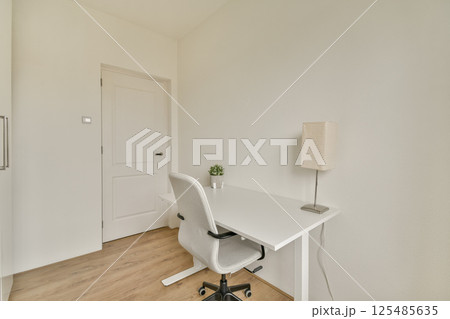 A sleek and minimalist home office featuring a white desk, ergonomic chair, and subtle decor aiming for a relaxing yet productive atmosphere. 125485635