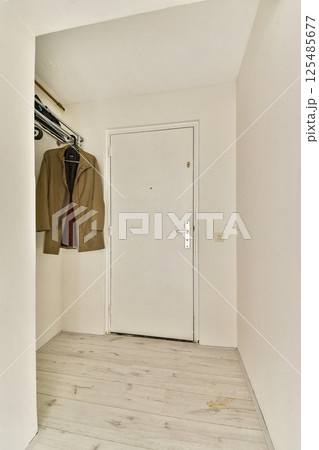 A clean and simple entryway featuring light-colored walls, a coat hanging on a rack, and a bright door. The minimalist style emphasizes functionality and space. A clean and simple entryway featuring light-colored walls, a coat hanging on a rack, and a bright door. The minimalist style emphasizes functionality and space. 125485677