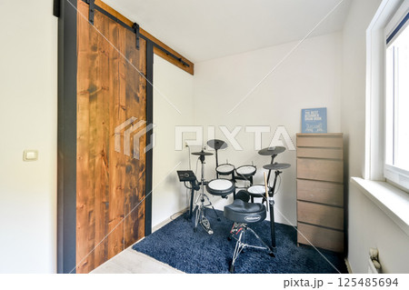 A stylish home room featuring an electronic drum set against a wooden sliding door and a neutral wall, complemented by a storage cabinet and plush rug. A stylish home room featuring an electronic drum set against a wooden sliding door and a neutral wall, complemented by a storage cabinet and plush rug. 125485694