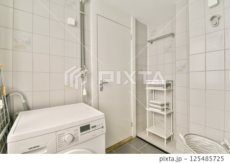 A sleek and modern laundry room featuring a washing machine, minimalist decor, tiled walls, and organized shelving for an efficient workspace. 125485725