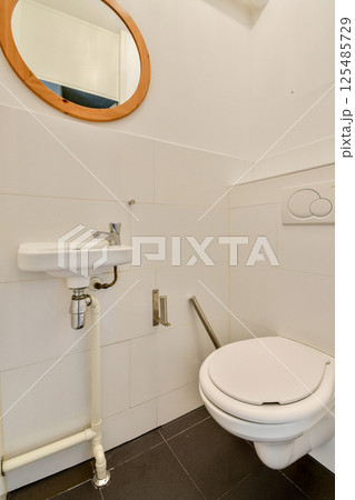 A sleek and minimalistic bathroom featuring a modern toilet, wall-mounted sink, and stylish circular mirror, emphasizing a contemporary aesthetic. A sleek and minimalistic bathroom featuring a modern toilet, wall-mounted sink, and stylish circular mirror, emphasizing a contemporary aesthetic. 125485729