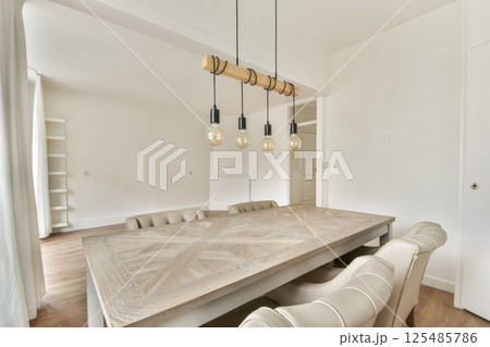 A stylish modern dining room featuring a wooden table and distinctive pendant lights hanging from the ceiling, creating an inviting atmosphere. 125485786