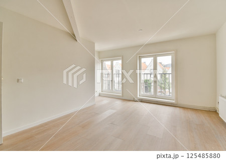 A bright and airy modern room showcasing large windows that offer a view of the outside. The wooden flooring adds warmth to the minimalist space. 125485880