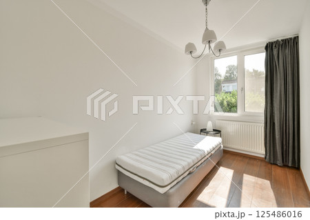 A bright and airy minimalist bedroom featuring a simple bed, large windows, and neutral tones. Perfect for relaxation and tranquility. 125486016