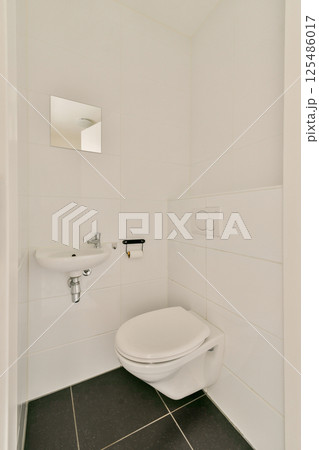 A sleek and modern bathroom featuring white tiled walls, a minimalist toilet, and small sink. The design emphasizes simplicity and clean lines. 125486017