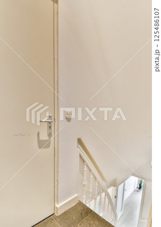 A sleek and modern interior featuring a stylish staircase leading to a door. The walls and flooring contribute to a minimalist and elegant aesthetic. A sleek and modern interior featuring a stylish staircase leading to a door. The walls and flooring contribute to a minimalist and elegant aesthetic. 125486107