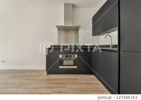 A sleek modern kitchen featuring dark cabinets, a stylish vent hood, and a minimalist aesthetic. The clean lines create an inviting and contemporary cooking space. 125486161