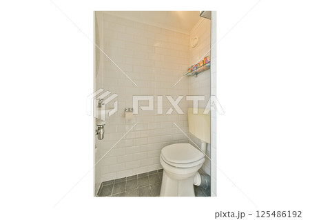 A compact bathroom featuring white tiled walls, a toilet, and a practical shelf for toiletries. The design emphasizes cleanliness and simplicity. 125486192