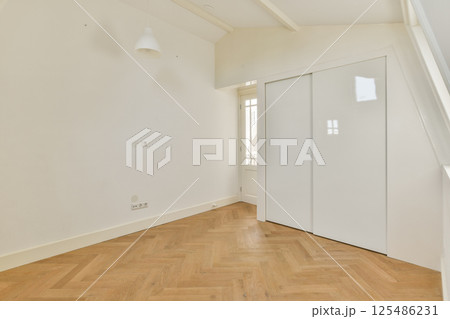 A spacious, minimalist room featuring wooden flooring and white walls. Natural light streams through the large window, enhancing the serene atmosphere. 125486231