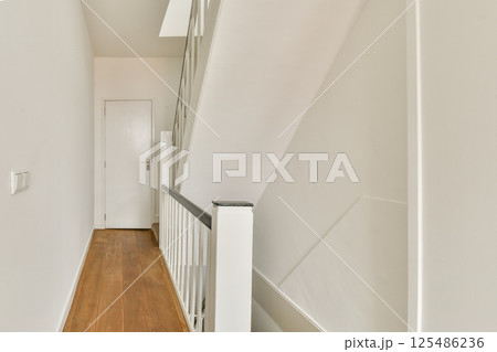 A minimalist hallway featuring a modern staircase, wooden flooring, and a clean white wall aesthetic, creating a spacious and bright atmosphere. A minimalist hallway featuring a modern staircase, wooden flooring, and a clean white wall aesthetic, creating a spacious and bright atmosphere. 125486236