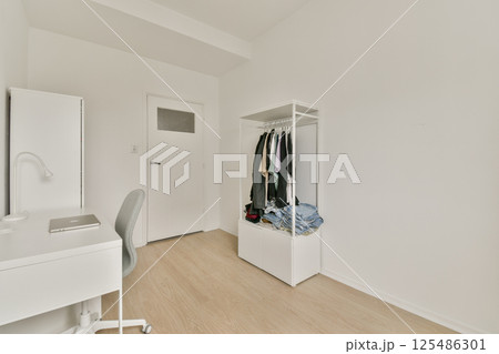 A sleek modern bedroom featuring minimalistic decor, light wood flooring, and an organized closet, creating a calm and spacious environment. 125486301