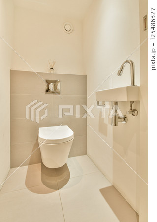 A sleek, minimalist bathroom featuring a contemporary toilet and a small sink against light-colored walls. The clean lines and simplicity create a modern aesthetic. 125486327