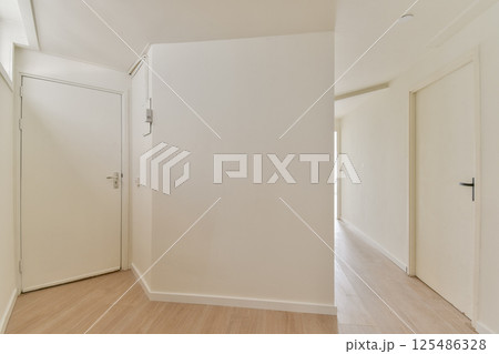 A serene and minimalist interior hallway featuring clean lines and neutral colors. The light wood flooring complements the bright walls. 125486328