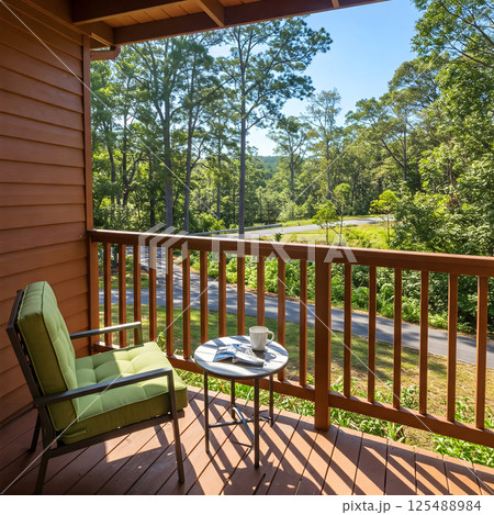 Wooden balcony with a green cushioned chair and small table overlooking a wooded landscape Wooden balcony with a green cushioned chair and small table overlooking a wooded landscape 125488984
