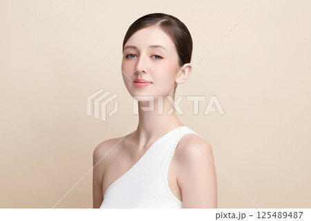 A beautiful young woman with clean, fresh skin against a beige background. Skincare, facial treatment, cosmetology, beauty, and spa. An elegant portrait of an woman. 125489487