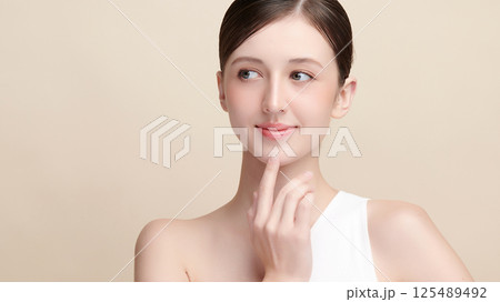 A beautiful young woman with clean, fresh skin against a beige background. Skincare, facial treatment, cosmetology, beauty, and spa. An elegant portrait of an woman. A beautiful young woman with clean, fresh skin against a beige background. Skincare, facial treatment, cosmetology, beauty, and spa. An elegant portrait of an woman. 125489492
