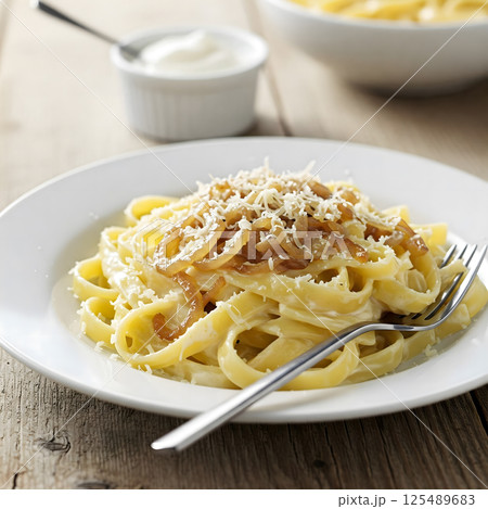 Linguine with caramelized onions and grated cheese on a white plate, with a small bowl of cream in the background Linguine with caramelized onions and grated cheese on a white plate, with a small bowl of cream in the background 125489683
