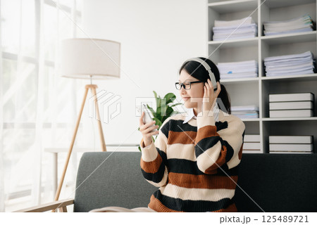 Smiling girl relaxing at home, she is playing music using smartphone tablet, and wearing white headphones. on sofa 125489721