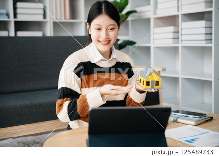 Asian woman working with House model real estate agent and customer discussing for contract to buy house, insurance or loan real estate consult concerning mortgage loan offer Asian woman working with House model real estate agent and customer discussing for contract to buy house, insurance or loan real estate consult concerning mortgage loan offer 125489733