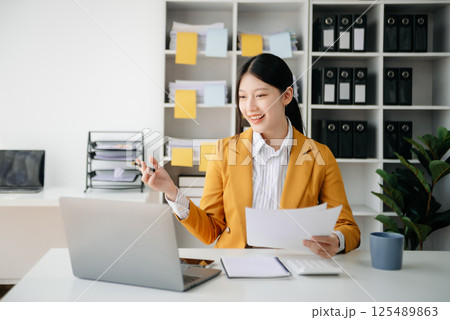 Confident Asian woman with a smile standing holding notepad and tablet at the modern office. Confident Asian woman with a smile standing holding notepad and tablet at the modern office. 125489863