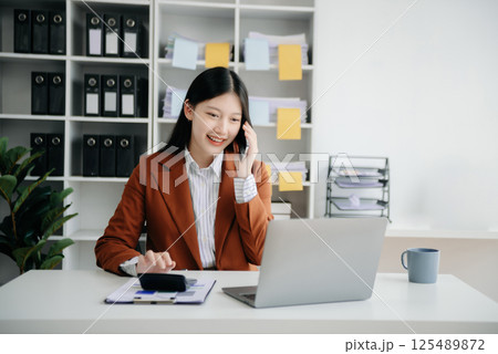 Business asian woman Talking on the phone and using a laptop with a smile while sitting in office 125489872