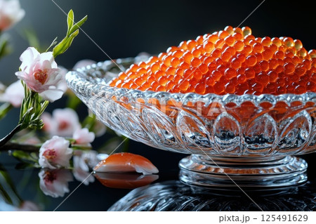Freshly prepared salmon roe displayed elegantly in a crystal bowl with delicate flowers on a glossy surface highlighting gourmet delicacy 125491629