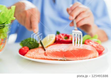 Asian elderly woman patient eating salmon stake and vegetable salad for healthy food in hospital. 125491886