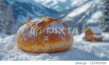 Freshly baked bread sits on pristine snow in a serene mountainous landscape with a cozy cabin in the background under a bright blue sky 125492426