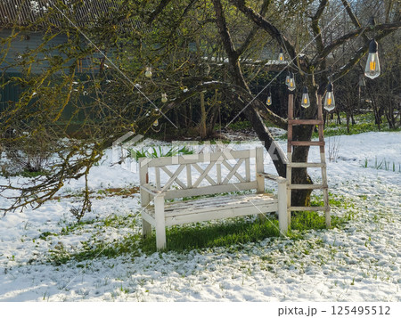 White bench, a ladder by an apple tree and a garland of LED lamps White bench, a ladder by an apple tree and a garland of LED lamps 125495512
