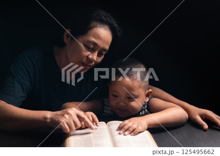 A mother teaches her child about Jesus Christ and the Christian faith, reading the Bible together and nurturing his belief in God. child, jesus christ, bible, christian, mother, person, faith, boy. 125495662