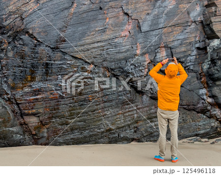 Caucasian male capturing rocky cliff texture in bright orange jacket Caucasian male capturing rocky cliff texture in bright orange jacket 125496118