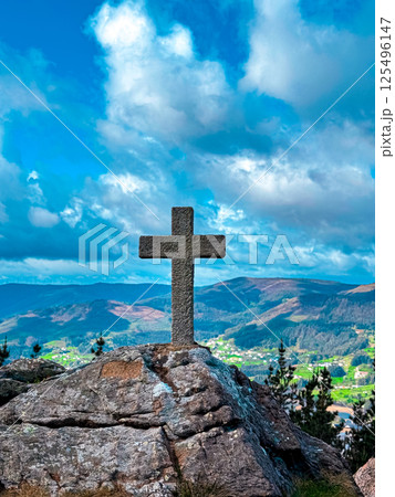 Stone cross on rocky cliff overlooking verdant landscape and dramatic sky 125496147