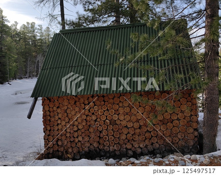 wooden hut with decorative cut logs and green roof, surrounded by snow in winter forest. 125497517