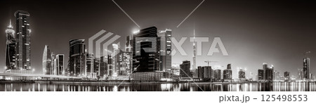 Urban city skyline with illuminated skyscrapers and waterfront railing in black and white at night, Dubai Marina bay UAE 125498553
