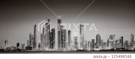 Urban city skyline with illuminated skyscrapers and waterfront railing in black and white at night, Dubai Marina bay UAE Urban city skyline with illuminated skyscrapers and waterfront railing in black and white at night, Dubai Marina bay UAE 125498588