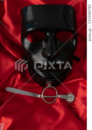 Adult sex games. Kinky lifestyle. Wartenberg Wheel and black mask on the red linen. Bdsm outfit 125498792