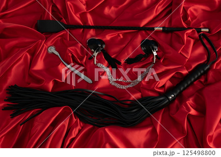 Adult sex games. Kinky lifestyle. Spank and whip ridding crop on the red linen. Bdsm outfit 125498800