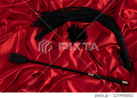 Adult sex games. Kinky lifestyle. Spank and whip ridding crop on the red linen. Bdsm outfit 125498802
