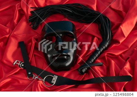 Adult sex games. Kinky lifestyle. Mask and whip ridding crop on the red linen. Bdsm outfit 125498804