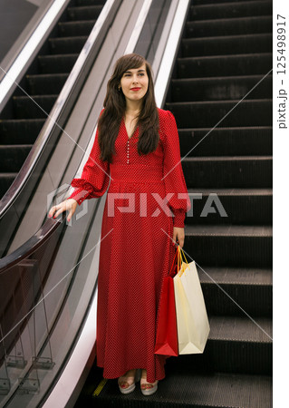 Happy woman with shopping bags on escalator. Shopping mall lifestyle and sales concept. Happy woman with shopping bags on escalator. Shopping mall lifestyle and sales concept. 125498917