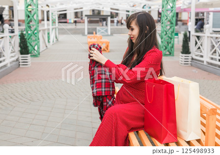 Woman smiles while reaching into shopping bag. Joy of shopping and discovering new purchases 125498933