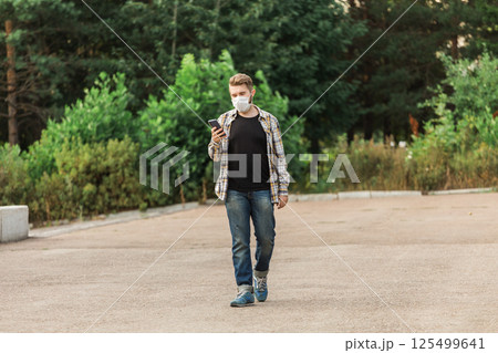 Man wearing a mask while walking in the park and checking his smartphone. Concept of modern life, health safety, and communication during pandemic times. Copy space Man wearing a mask while walking in the park and checking his smartphone. Concept of modern life, health safety, and communication during pandemic times. Copy space 125499641