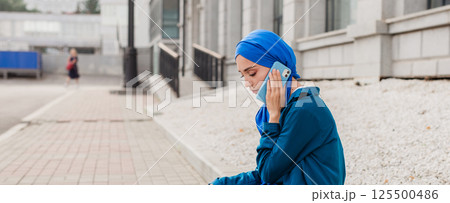 Young muslim woman in hijab speaking on the phone in urban surroundings. Communication, technology, and cultural diversity concepts. Banner with copy space Young muslim woman in hijab speaking on the phone in urban surroundings. Communication, technology, and cultural diversity concepts. Banner with copy space 125500486