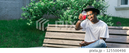 African american man enjoying a refreshing drink outdoors. Relaxation, leisure, and summer refreshment concepts. Banner with copy space African american man enjoying a refreshing drink outdoors. Relaxation, leisure, and summer refreshment concepts. Banner with copy space 125500498
