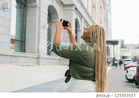 Affrican american woman taking a photo of a building with her smartphone. Tourism, sightseeing, and urban exploration moments 125501037