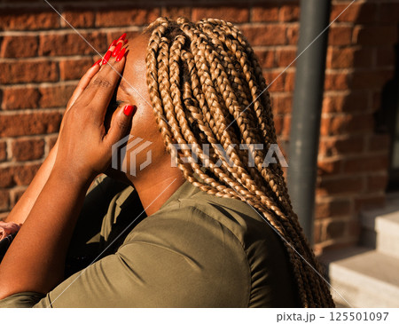 African american woman covering her face with her hands in bright sunlight outdoors. Emotion, fatigue, and real human moments of vulnerability. African american woman covering her face with her hands in bright sunlight outdoors. Emotion, fatigue, and real human moments of vulnerability. 125501097