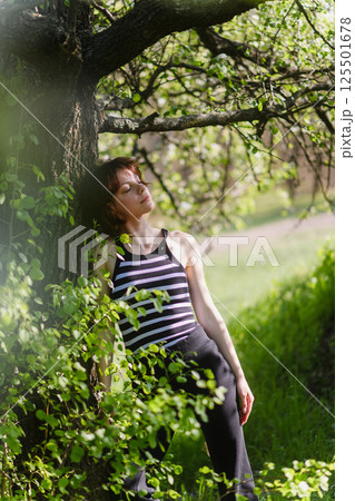 Young woman relaxing by tree in sunny spring forest. 125501678
