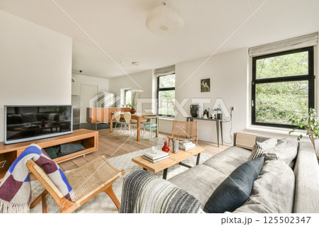 A stylish and inviting living room featuring contemporary furniture, large windows offering natural light, and a blend of textures for a cozy ambiance. 125502347