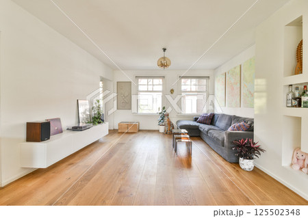 A spacious, modern living room featuring minimalist decor, natural light, and elegant furnishings. The wooden floor and vibrant artwork enhance the inviting atmosphere. 125502348