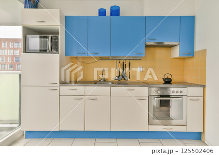 A contemporary kitchen featuring sleek blue cabinetry, a stainless steel oven, and modern appliances, perfect for functional cooking spaces. A contemporary kitchen featuring sleek blue cabinetry, a stainless steel oven, and modern appliances, perfect for functional cooking spaces. 125502406